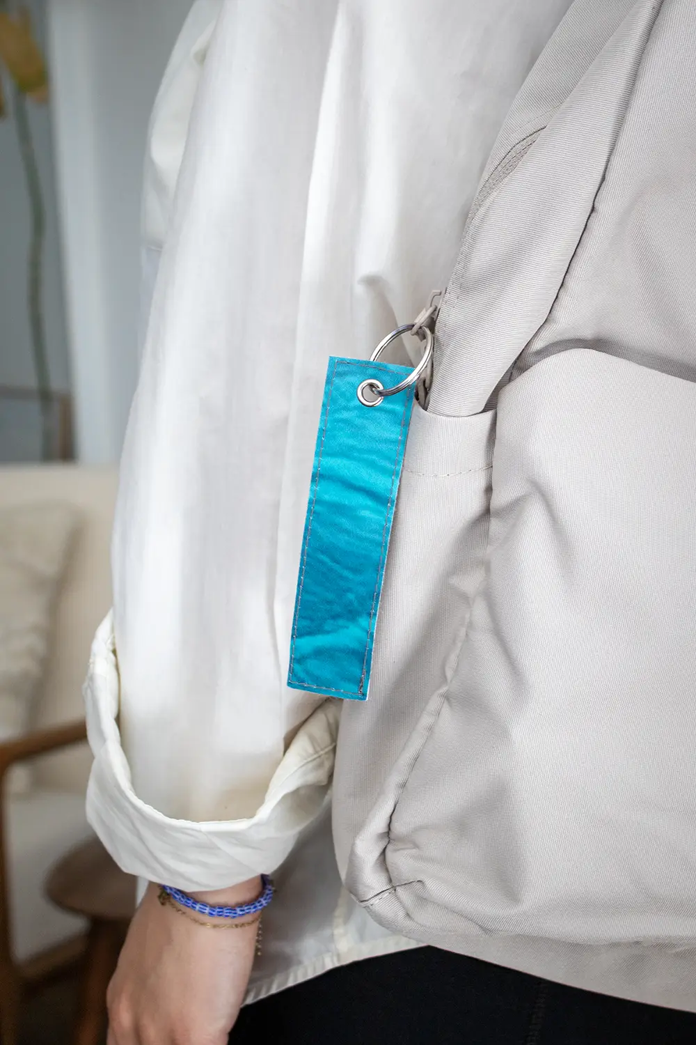 Llavero hecho con lona reciclada azul colgando de la cremallera de una mochila gris