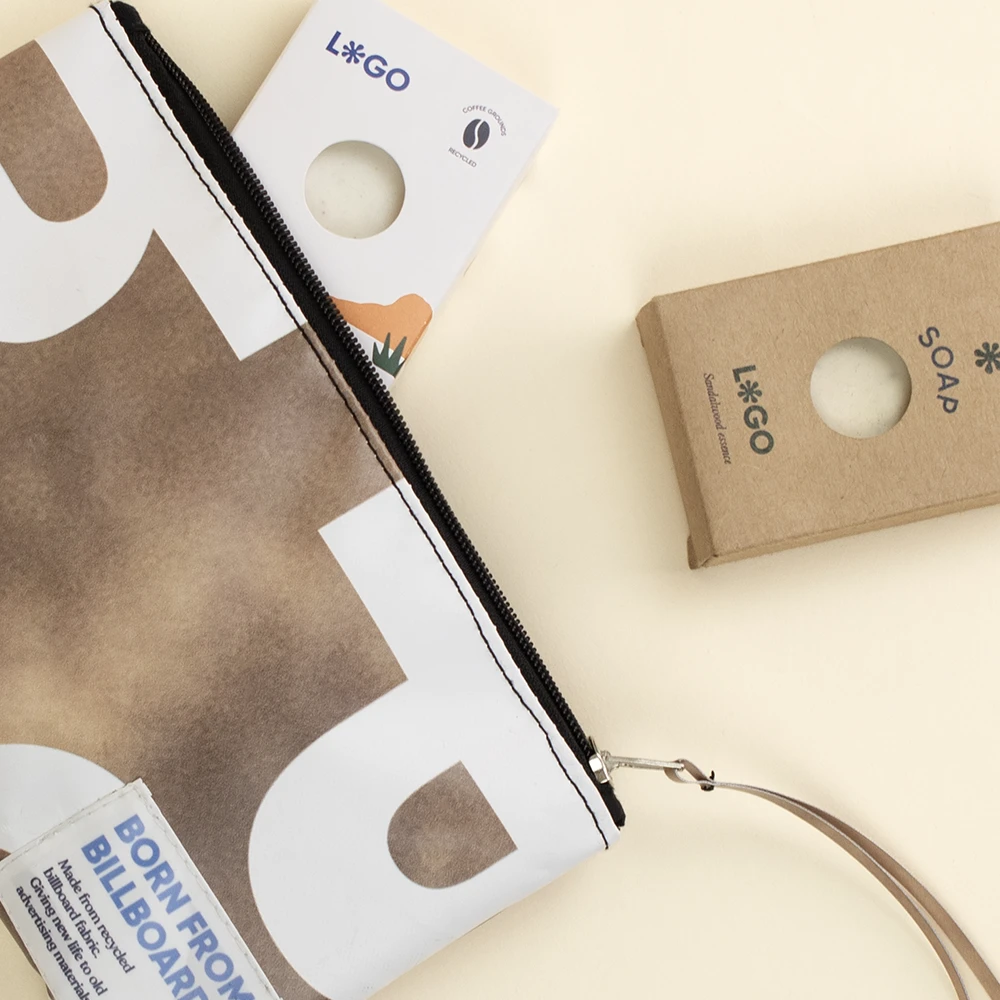 Neceser de lona reciclada MOMO Neceser de lona reciclada de color marrón y blanco con la cremallera abierta junto a dos cajas de jabones