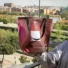 Chica mostrando a cámara una tote bag de lona reciclada roja con asas negras con la ciudad de fondo