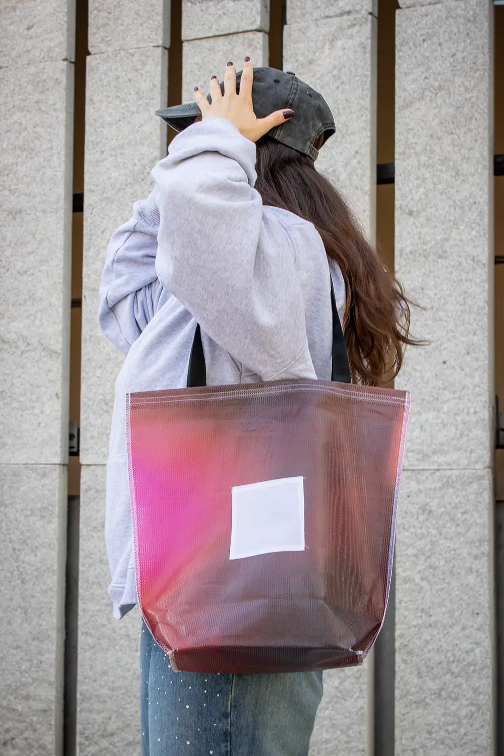 Chica en la calle llevando una tote bag de lona reciclada roja colocándose una gorra negra en la cabeza