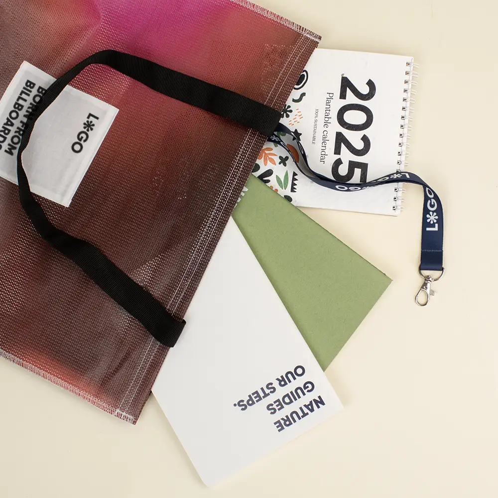 Tote bag de lona reciclada roja con asas negras con un calendario de 2025, un lanyard, un cuaderno verde y un cuaderno blanco