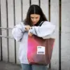 Chica en la calle llevando una tote bag de lona reciclada roja con asas negras