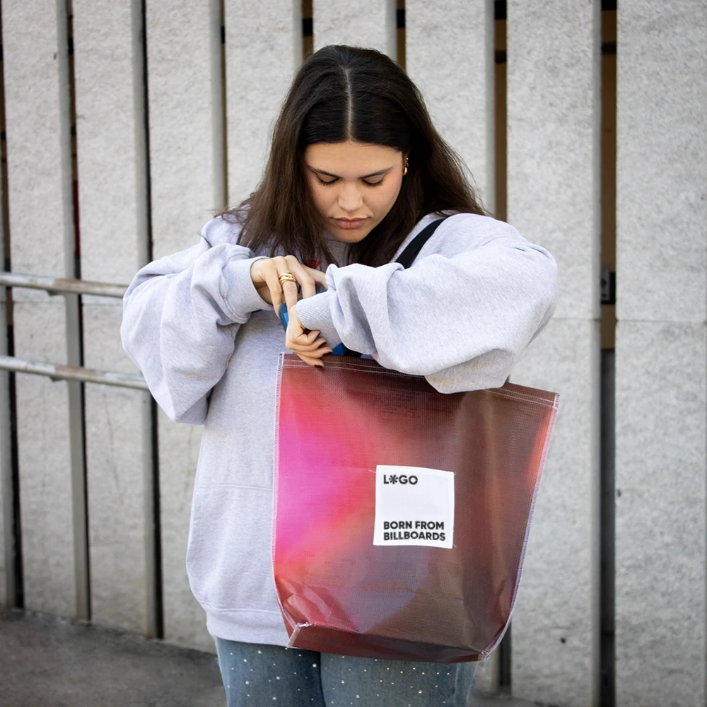 Chica en la calle llevando una tote bag de lona reciclada roja con asas negras