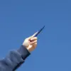 Mano alzando bolígrafo de aluminio azul con el cielo de fondo