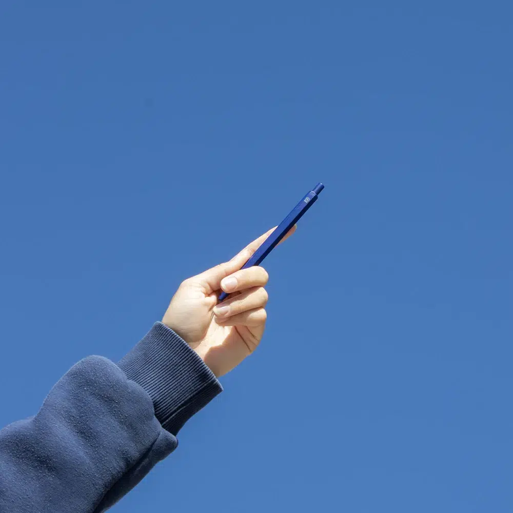 Mano alzando bolígrafo de aluminio azul con el cielo de fondo
