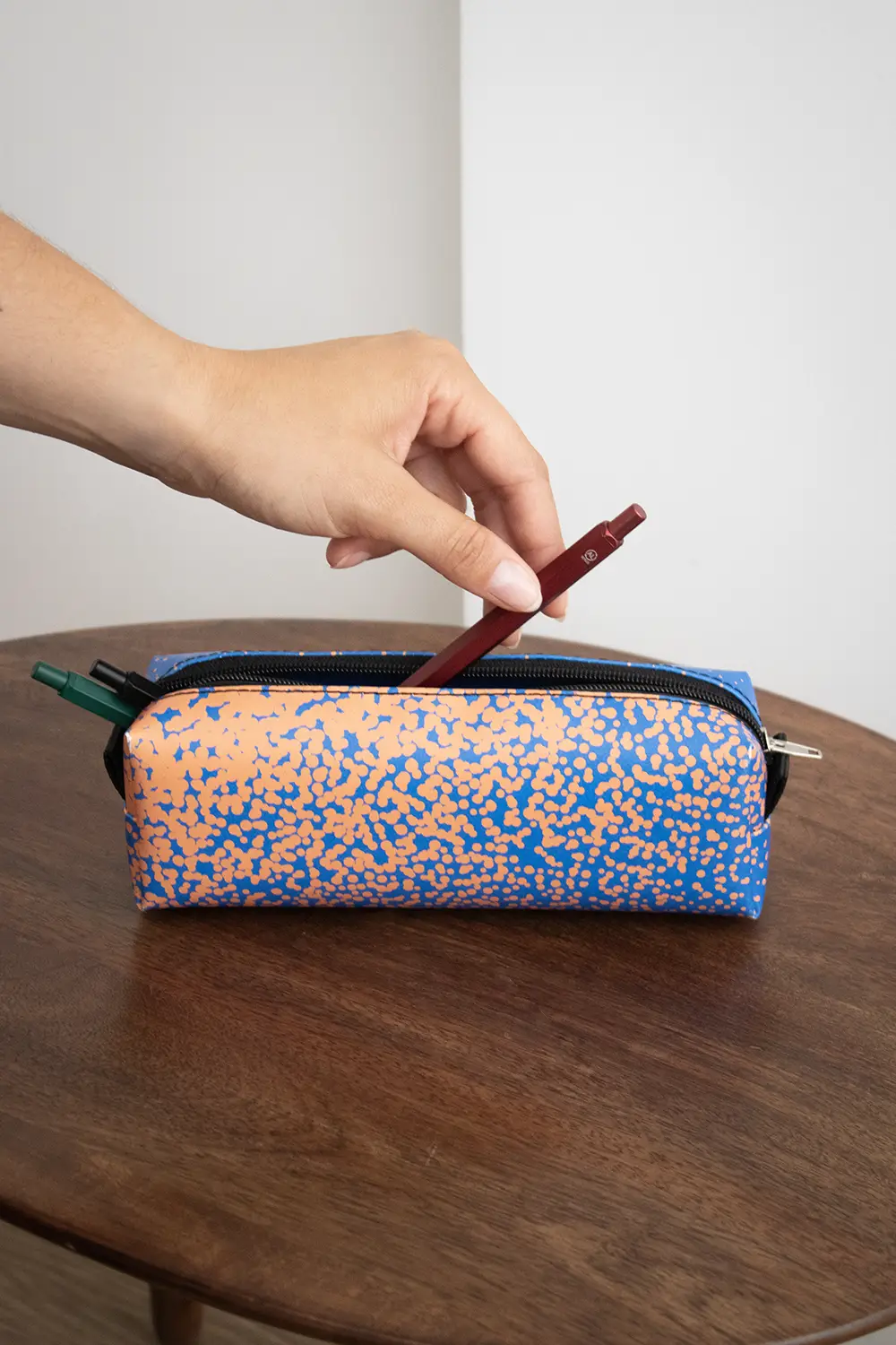 Mano introduciendo bolígrafo de aluminio rojo en un estuche