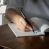 Mano escribiendo sobre un cuaderno con bolígrafo de aluminio negro sobre una superficie de madera