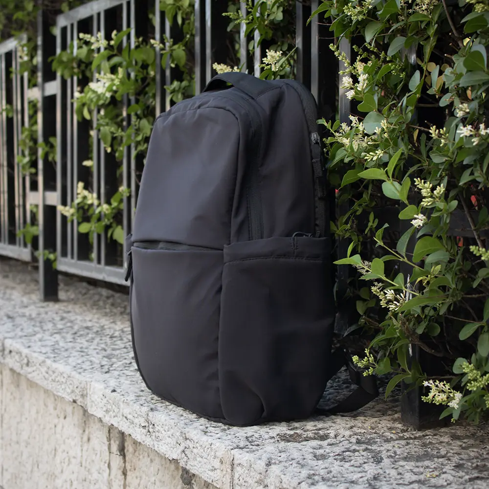 Mochila urbana personalizada negra sobre bordillo con arbustos