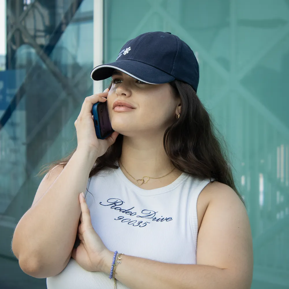 Chica hablando por teléfono con una gorra azul con logo lateral