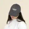 Chica con una gorra gris con logo frontal en un fondo beige