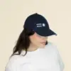 Chica con una gorra azul con logo lateral en un fondo beige