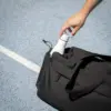 Bolsa de deporte PULSE Mano cogiendo una botella blanca de una bolsa de deporte negra de poliƩster reciclado.
