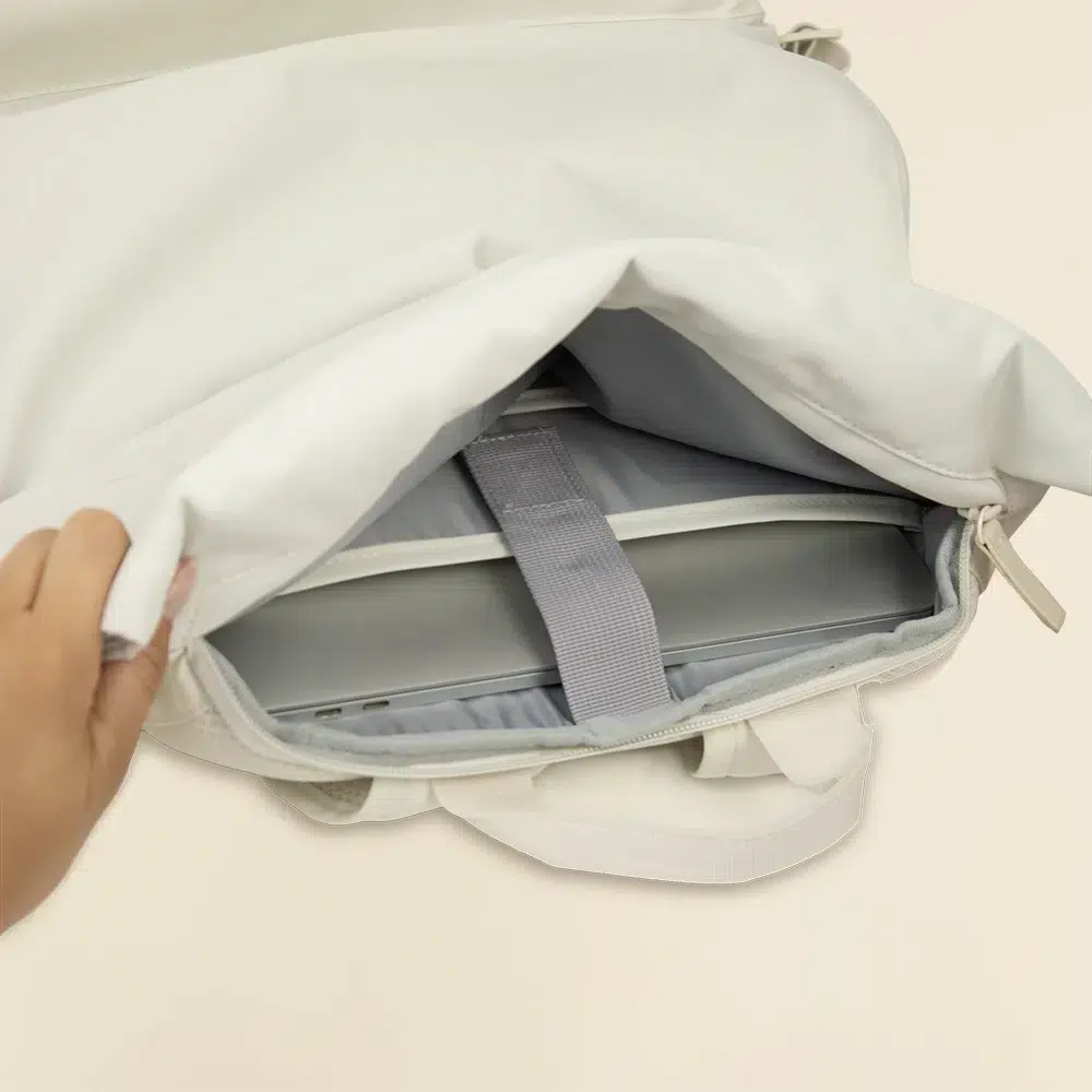 Mano abriendo mochila roll top blanca con un portátil dentro