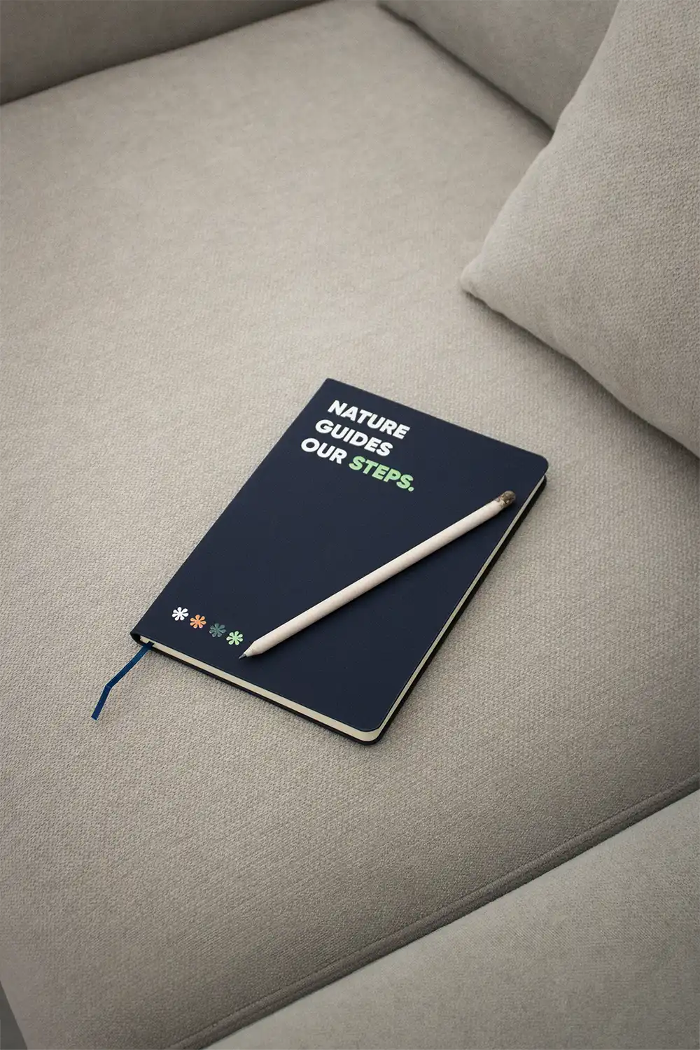 Cuaderno ecológico personalizado azul junto con un lápiz sobre un sofá gris