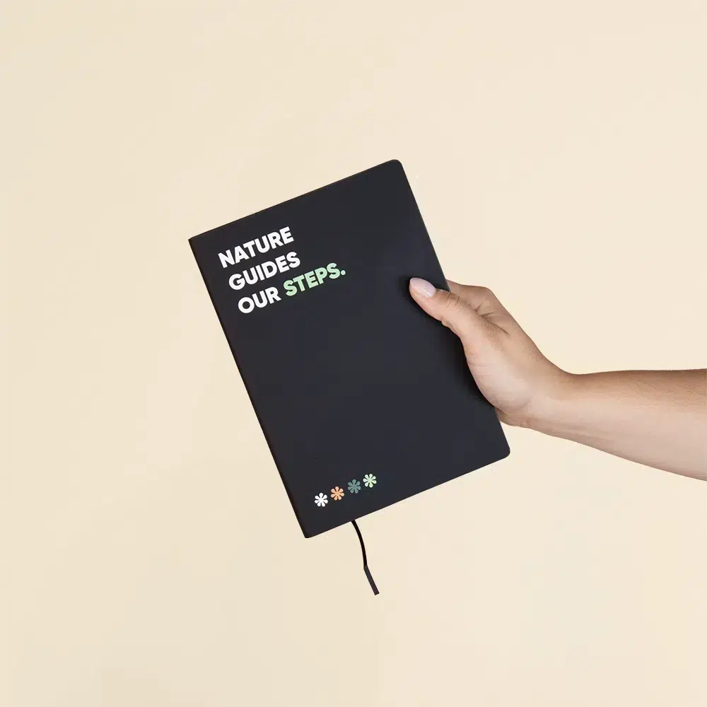 Mano sosteniendo un cuaderno ecológico personalizado negro sobre fondo beige