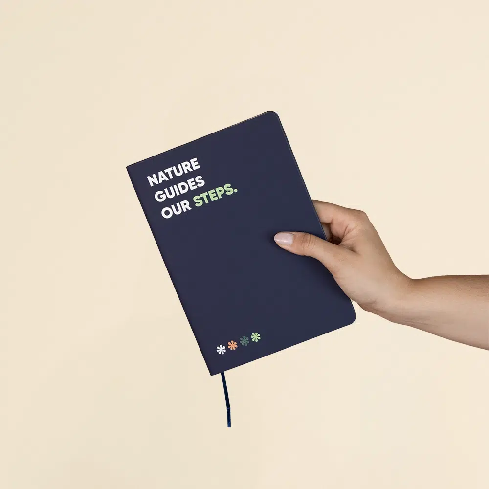 Mano sosteniendo un cuaderno ecológico personalizado azul sobre fondo beige