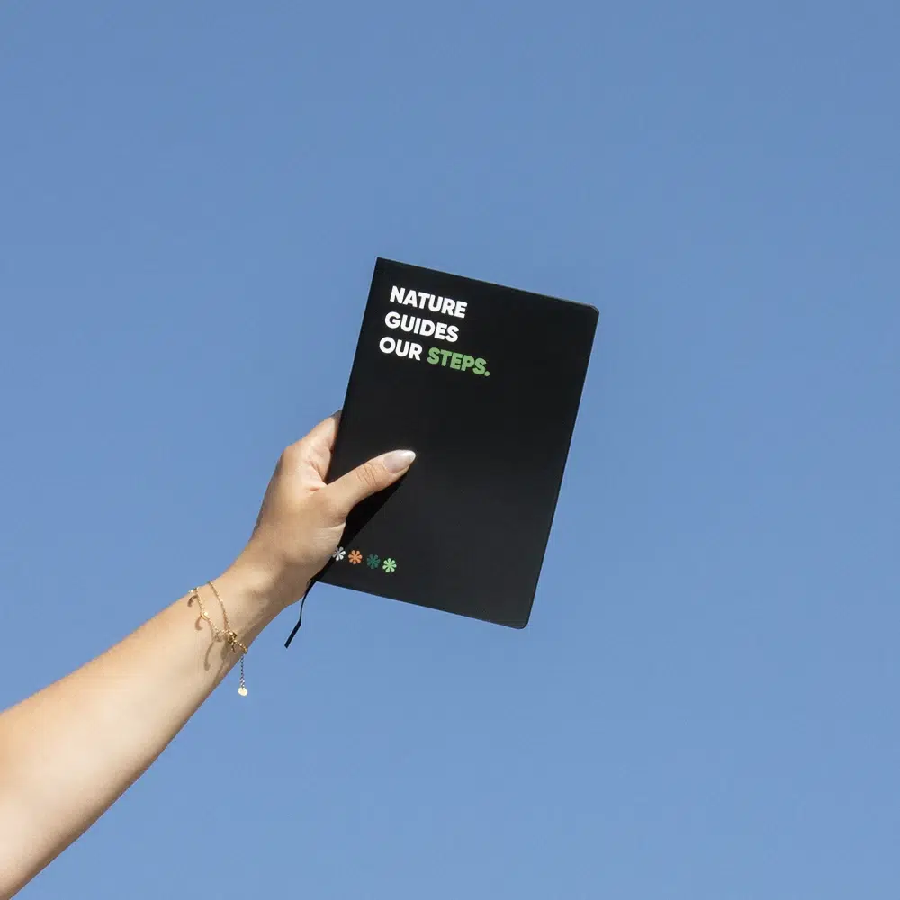 Mano alzando al cielo un cuaderno ecológico personalizado negro