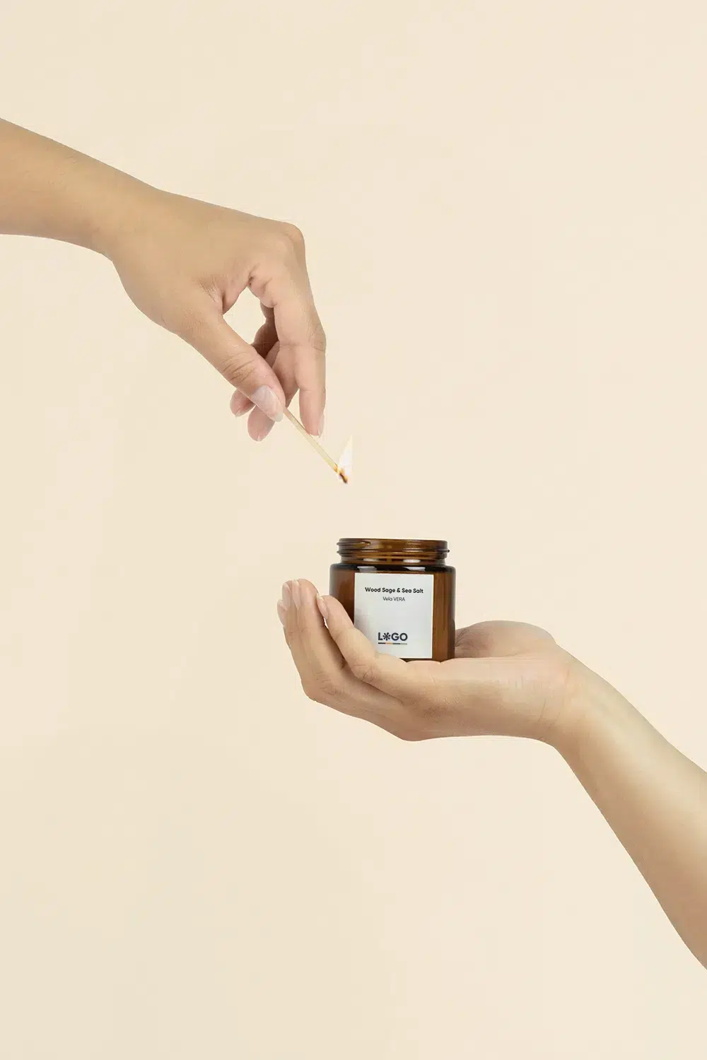 Manos sosteniendo y encendiendo con cerilla una vela aromática personalizada sobre un fondo beige