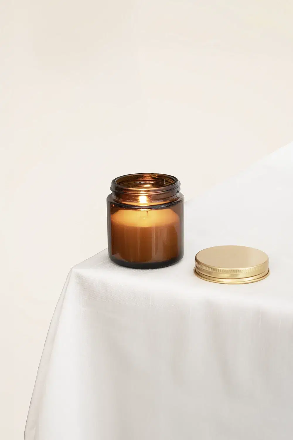 Vela aromática personalizada con tapa metálica sobre una mesa con mantel blanco
