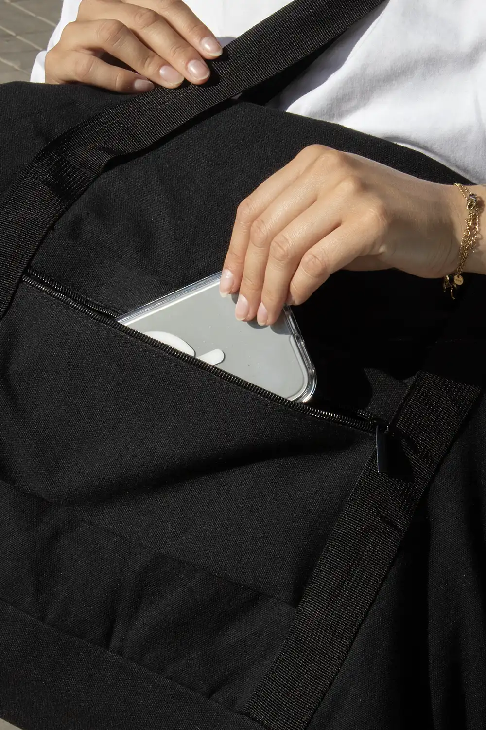 Mano guardando un móvil en una bolsa negra de viaje de algodón y poliéster reciclado