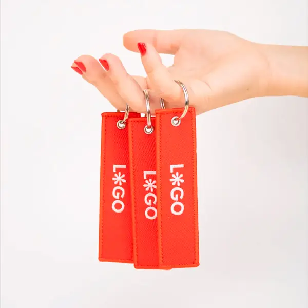 Mano sujetando 3 llaveros de tela rojos personalizados con logo blanco