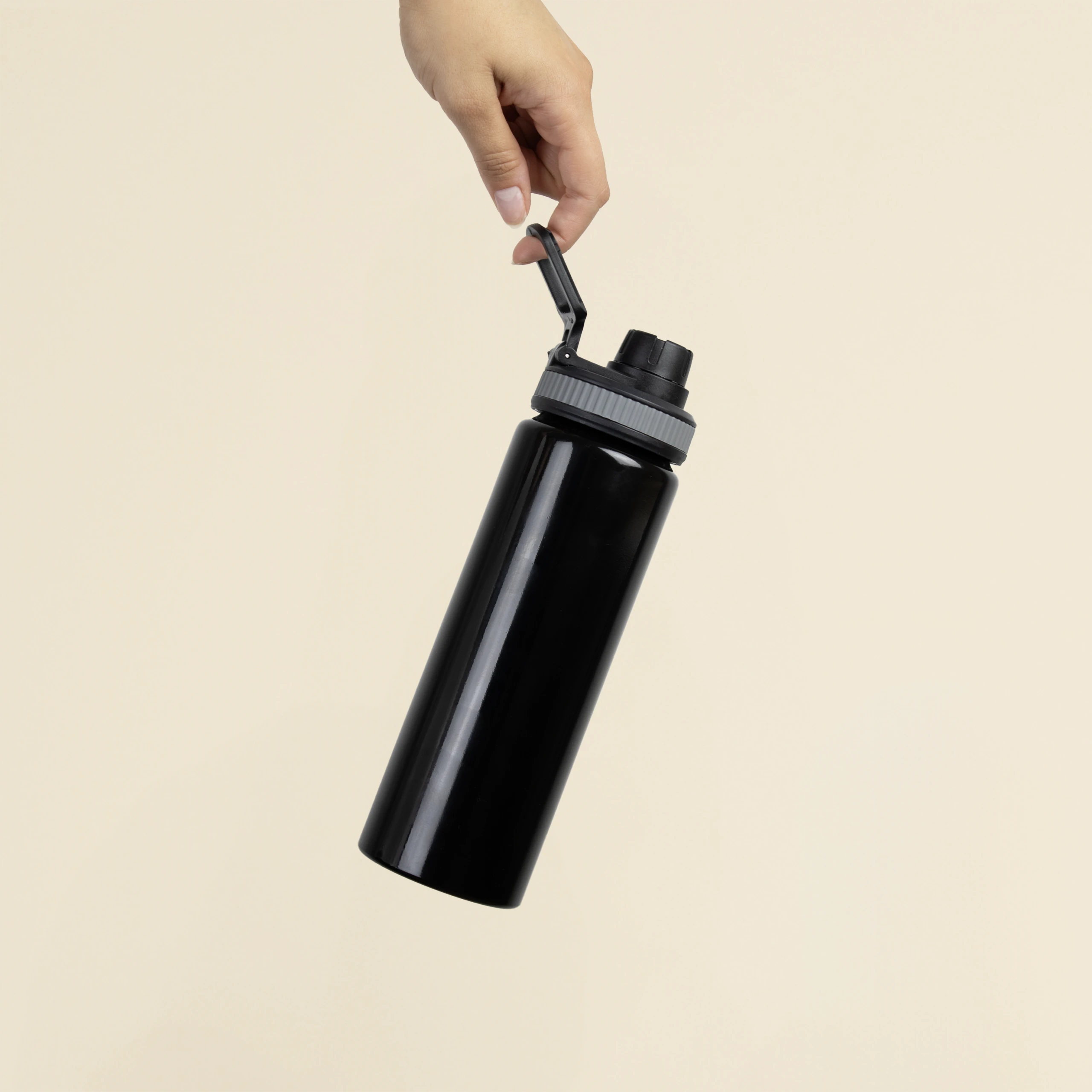 Mano sosteniendo una botella deportiva negra personalizada en aluminio reciclado sobre un fondo beige