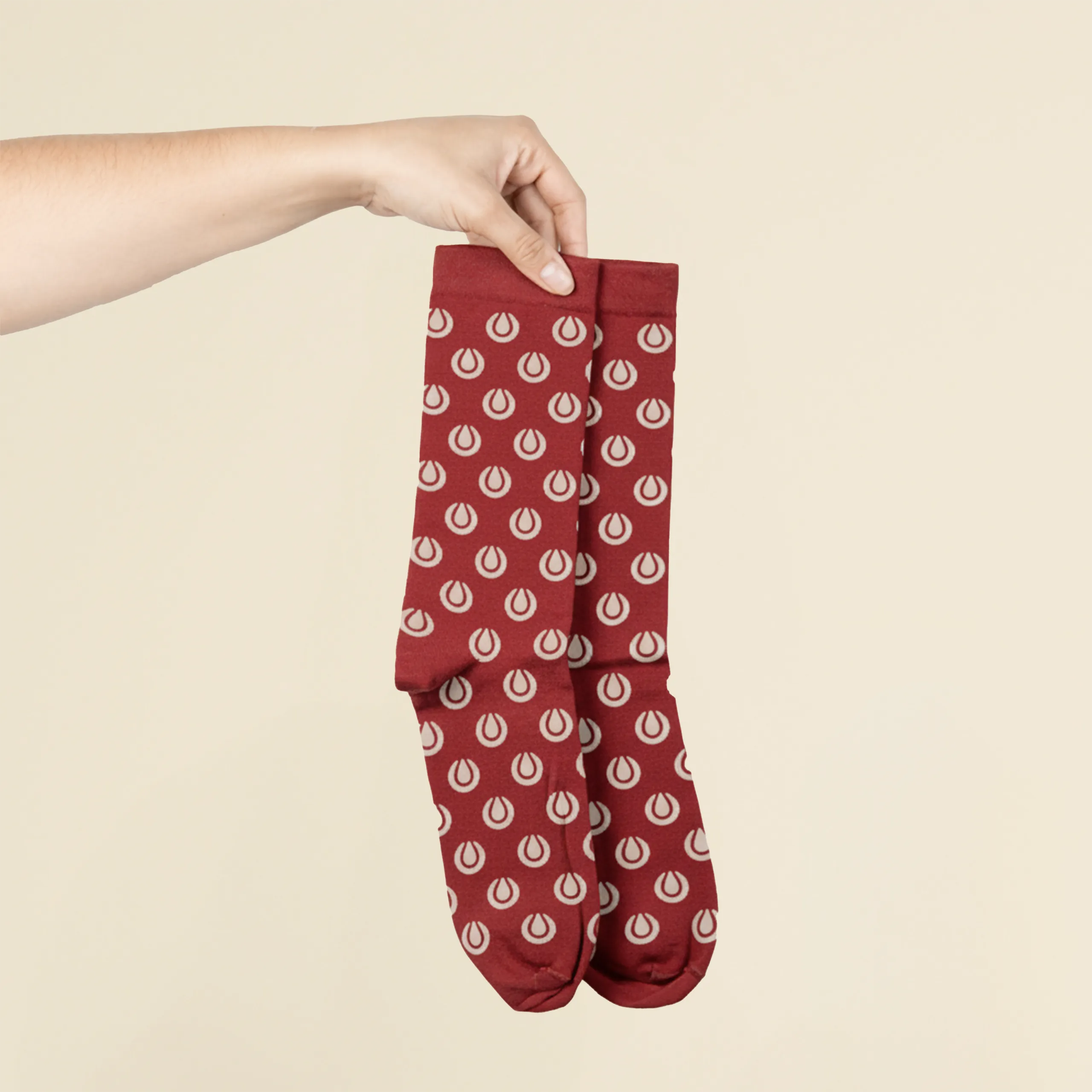 Manos sosteniendo unos calcetines rojos personalizados con logo sobre un fondo beige